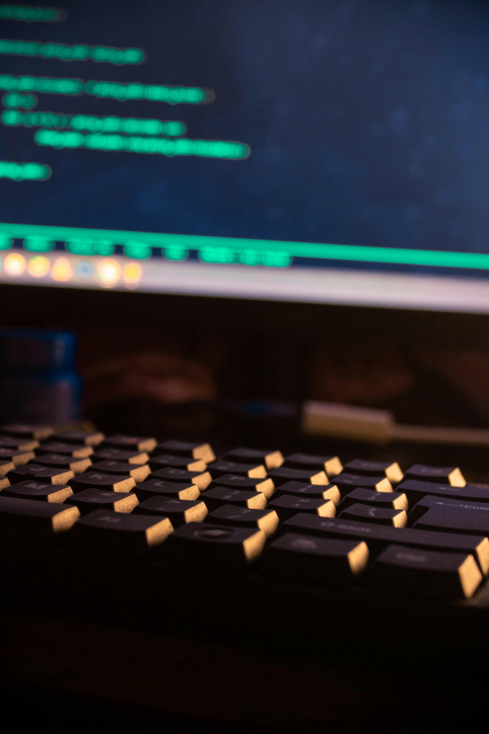 A focused view of a computer keyboard and a monitor displaying code, highlighting technology use.